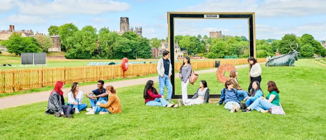 Students on grass with trees and cathedral in the distance