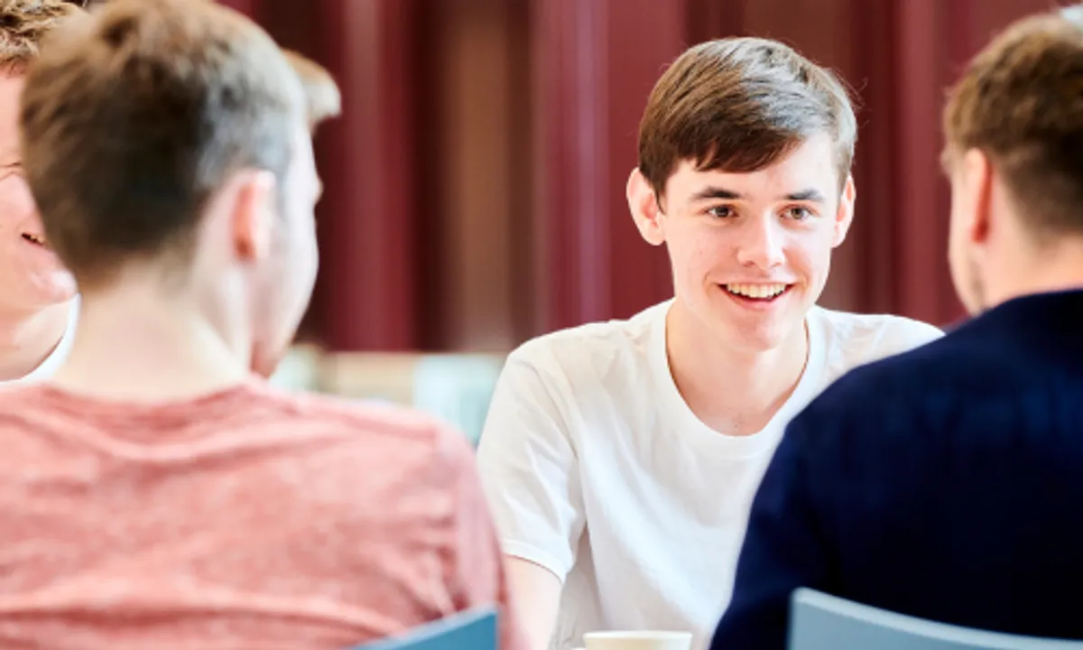 A male student chatting with two other males with their back to us