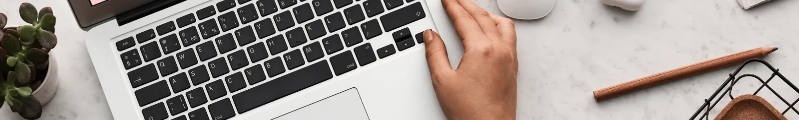 hands on a laptop keyboard with a plant, pencil and basket in view.