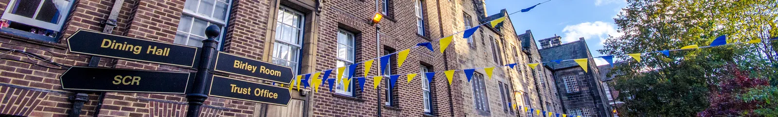 Hatfield College grounds with signpost in the foreground and blue and yellow bunting hung in the background