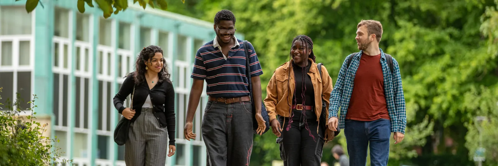 A group of four students walking together. They are talking to each other and smiling.