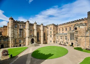 High stone buildings on two sides of a courtyard with a circular lawn in the centre and smaller areas of lawn against the sides.