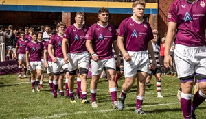 A line of male rugby players wearing purple tops walking out on to the pitch.