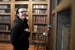 A student smiles as they look at the bookshelves in the historic library