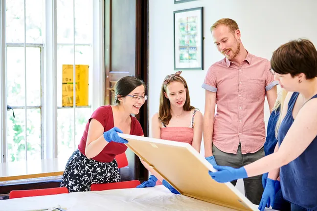 A group of people looking at a framed artwork on a table