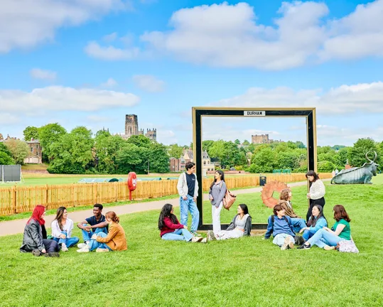 Groups of students sitting and standing on grass with Durham Cathedral in the background
