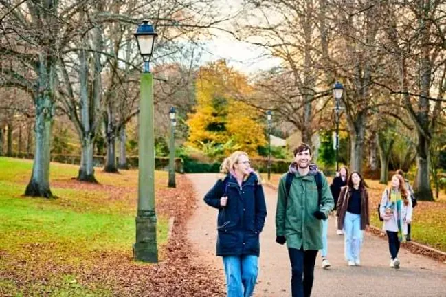 Two students walking on campus under autumnal trees
