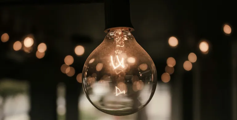 A bare lightbulb hangs in a dark space.