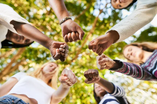 Group of people standing together in a circle with their fists together