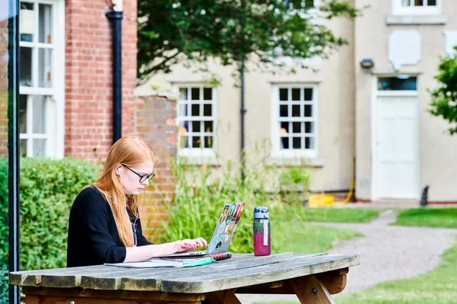 Student working on laptop at bench outside