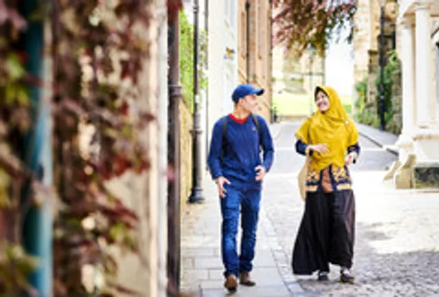 male student with blue cap and female student with yellow head dress walking along street