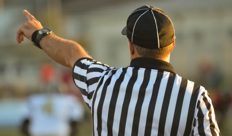 Image showing the back of a referee in a black and white stripey top with a black cap on with his left arm raised