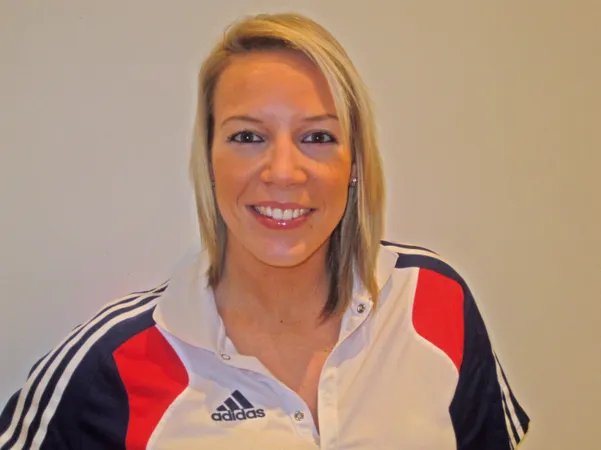 A blonde haired woman wearing a sports jacket smiling at the camera