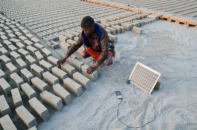 A man making bricks while solar charging phone
