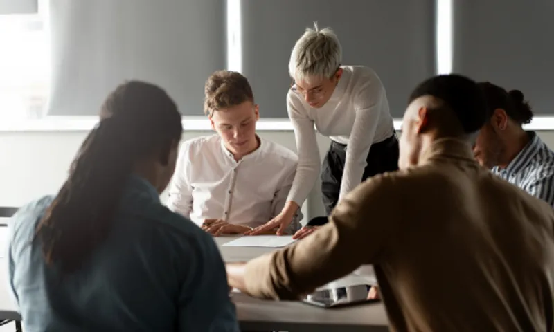 A student standing over another another student who is sitting reviewing a document