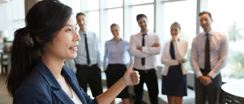 A female lecturer addresses standing business students in corridor