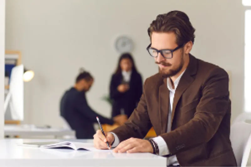 Academic man writing at desk with others in background