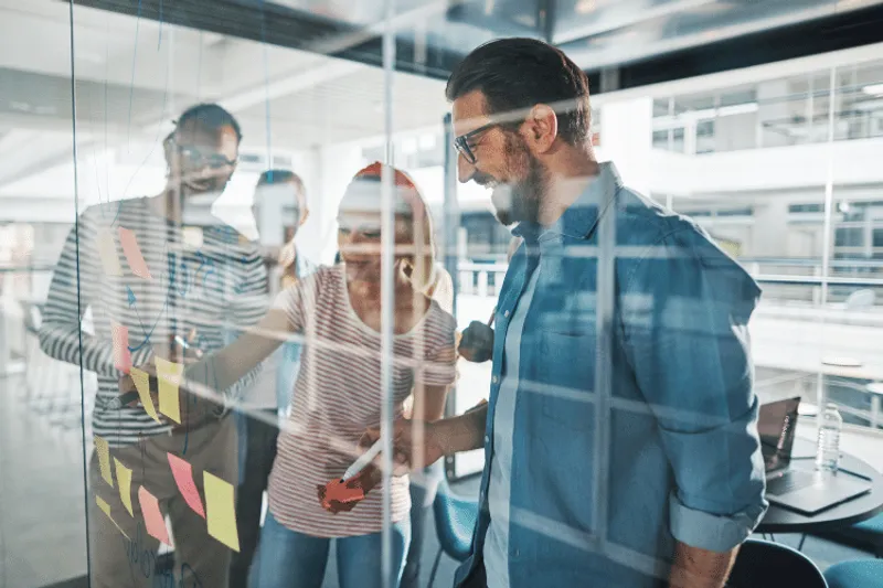 Group of people sticking notes onto a glass screen