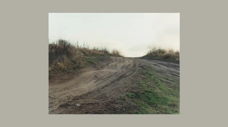 A dirt track rises from the lower left-hand side upwards towards the centre of the image. A smaller dirt track from the right-hand side comes up to join it in the centre. On each side of the track are sun-bleached grasses.