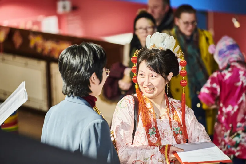 Person in traditional costume from China talks to a student musician (they have their back to the camera)