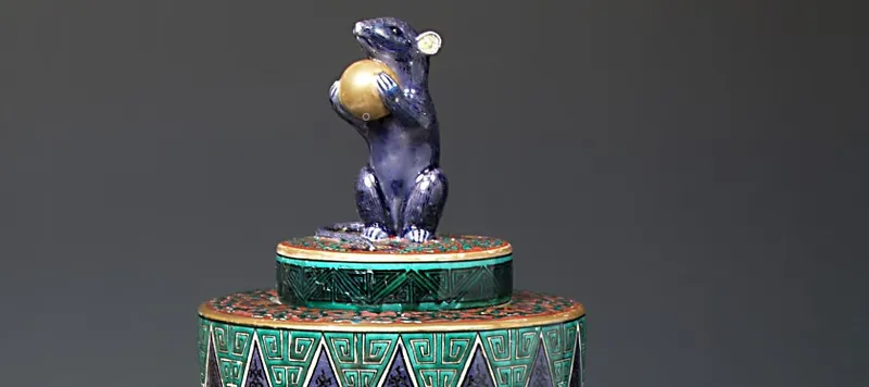 Ornament depicting a rat holding a ball and stood on a platform