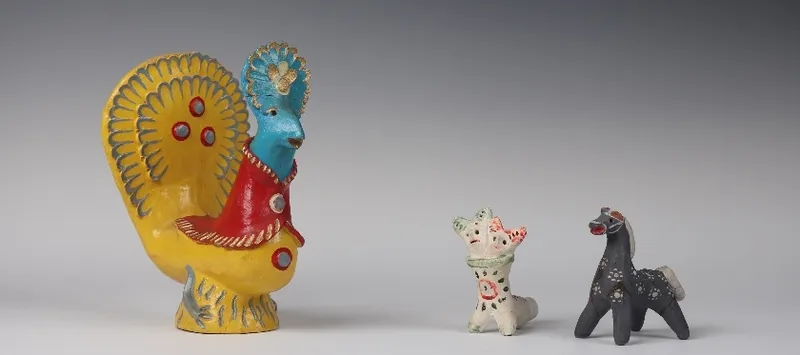 Group of three toys, one is a large yellow and blue rooster, and the smaller two are a black horse and a white fantasy creature with two heads.