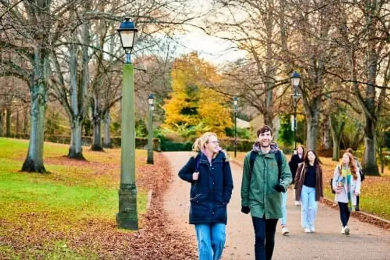 Two students walking on campus under autumnal trees