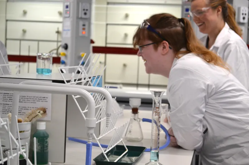 Two students in lab coats in one of our science labs eagerly watch their experiment