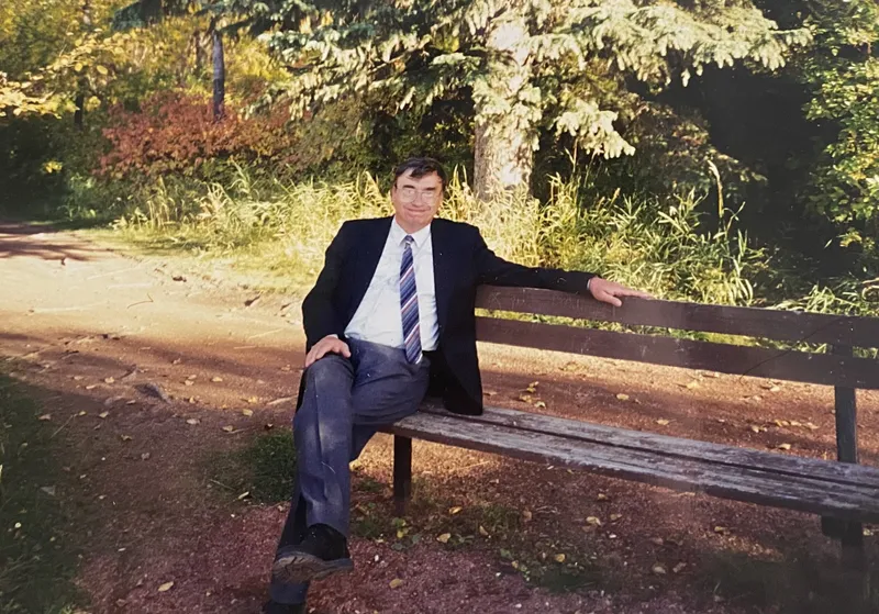 Dr Palmer sits on a bench with trees behind him.