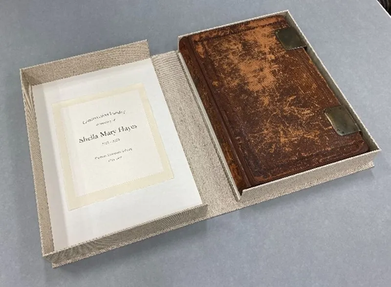 Images shows the first book of matriculation in a grey clamshell cover. the cover displays a dedication to Sheila Mary Hayes