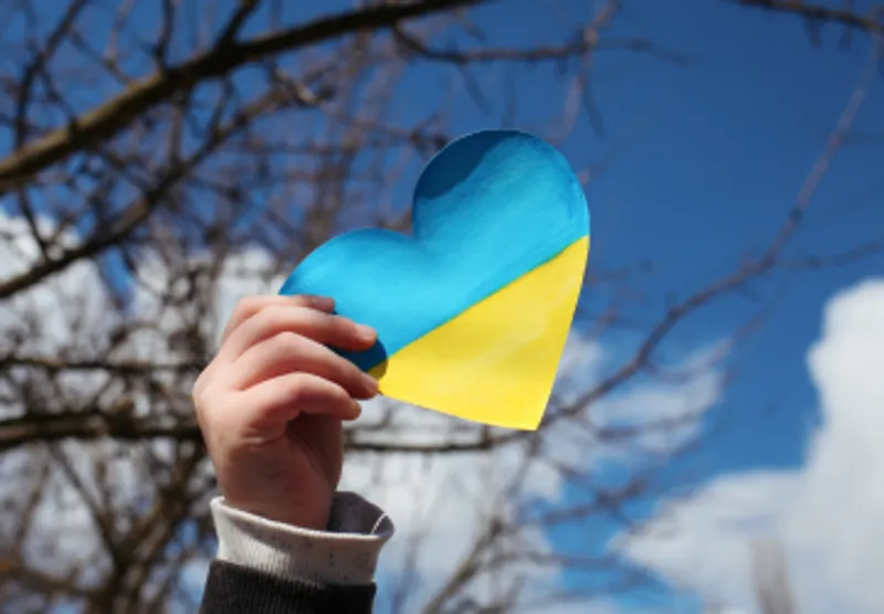 A hand holding a heart shaped Ukrainian flag