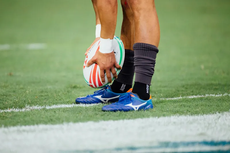 A close up of a rugby player holding a rugby ball above their feet
