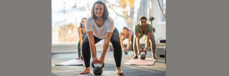 Gym class lifting handheld weights with smiling woman in foreground