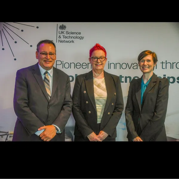 A male and two females in suits stood in a line smiling for a formal photograph