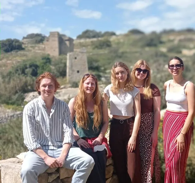 five people looking at the camera with the ancient site of Ghar Dalam in the background