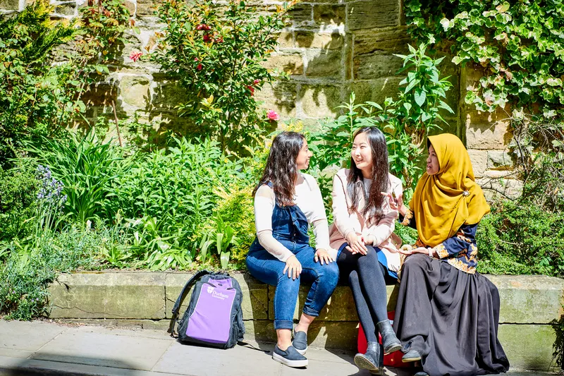 3 female students sitting on a wall chatting