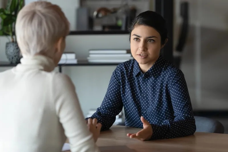 two people sitting on opposite sides of a desk talking