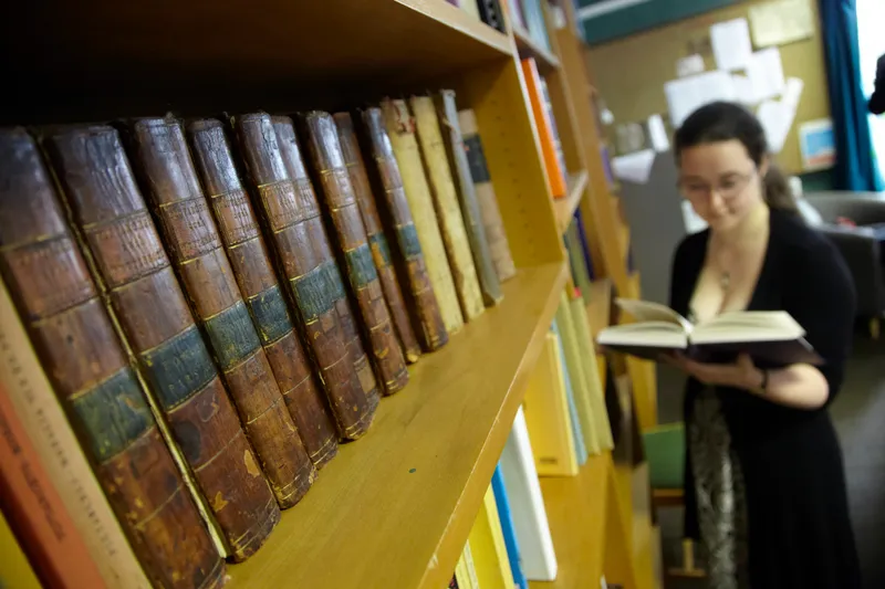 A student reading in the library, by a shelf of historic texts