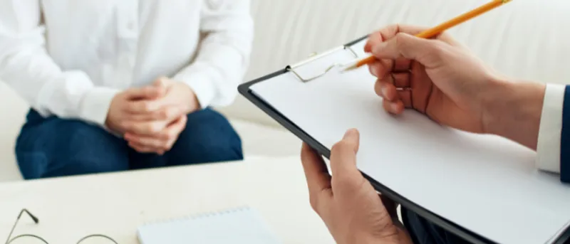 Male hands holding clipboard assessing seated woman