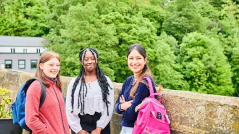 A picture of three female students standing in front of some trees.
