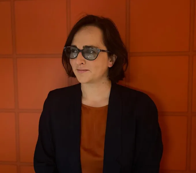 A woman in glasses stood against a red background