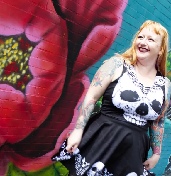 A person looking to the side smiling, standing in front of a wall decorated with artwork