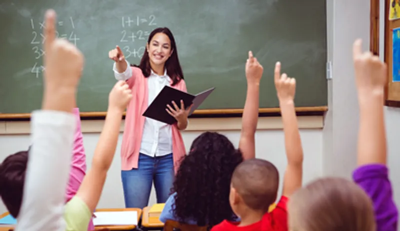 A classroom full of children holding their hands up to answer a question