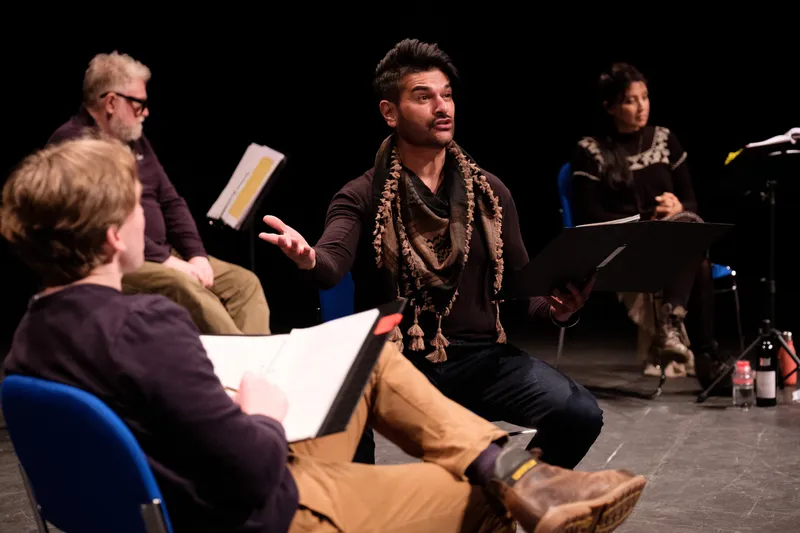 Photograph of a group of actors performing in a rehearsal in a theatre space.