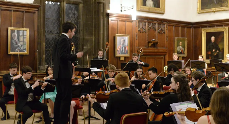 An orchestra playing in a room in Durham Castle with portraits on the walls