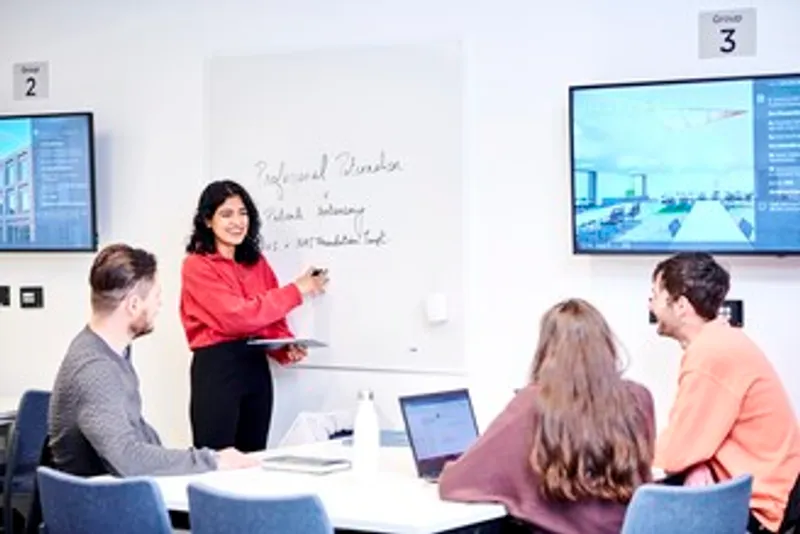 Female lecturer in front of a whiteboard, smiling at three students.