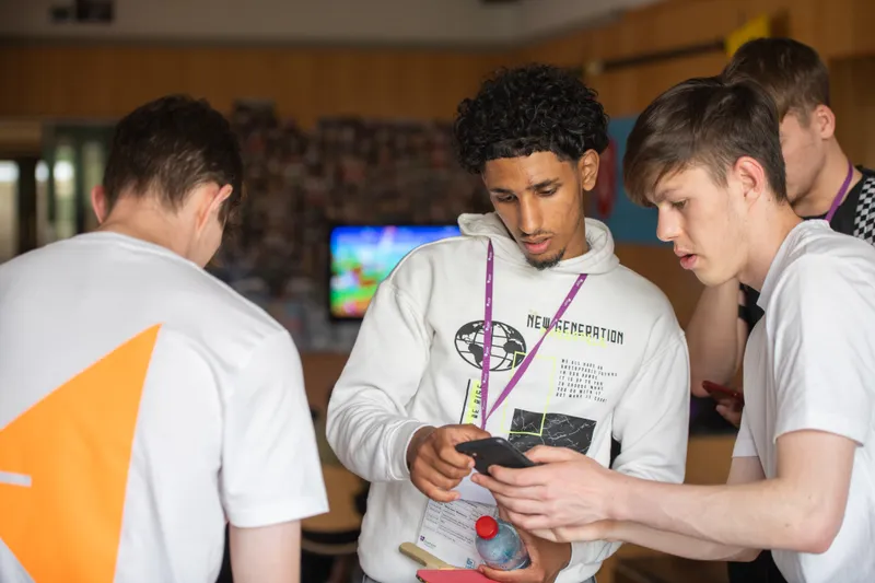 Three students around a table tennis table with two looking at a phone
