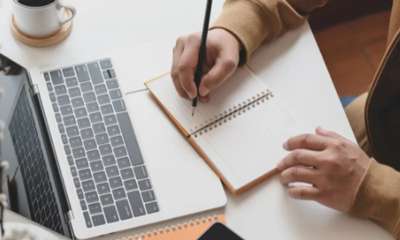 Laptop and mans hands writing in a notebook
