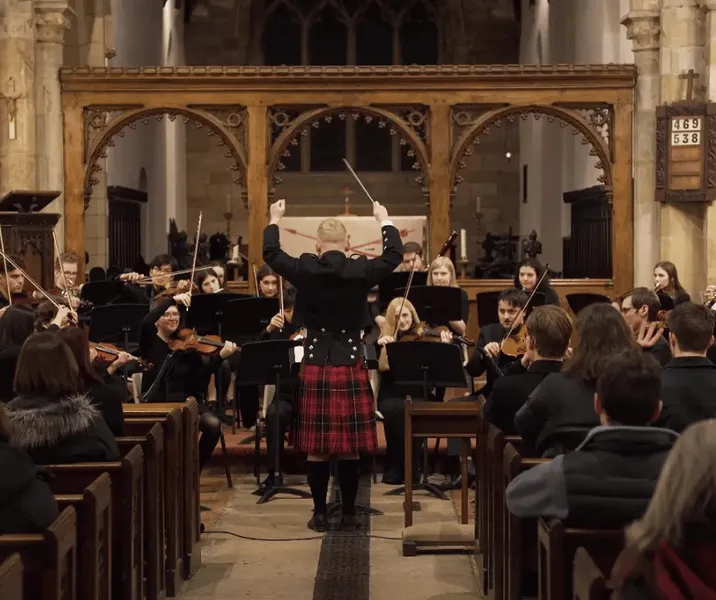 Classical Ensemble members performing in St Oswald's Church in front of their student conductor wearing a kilt.
