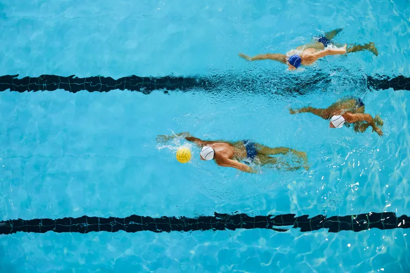 A group of male water polo swimmers swimming from left to right